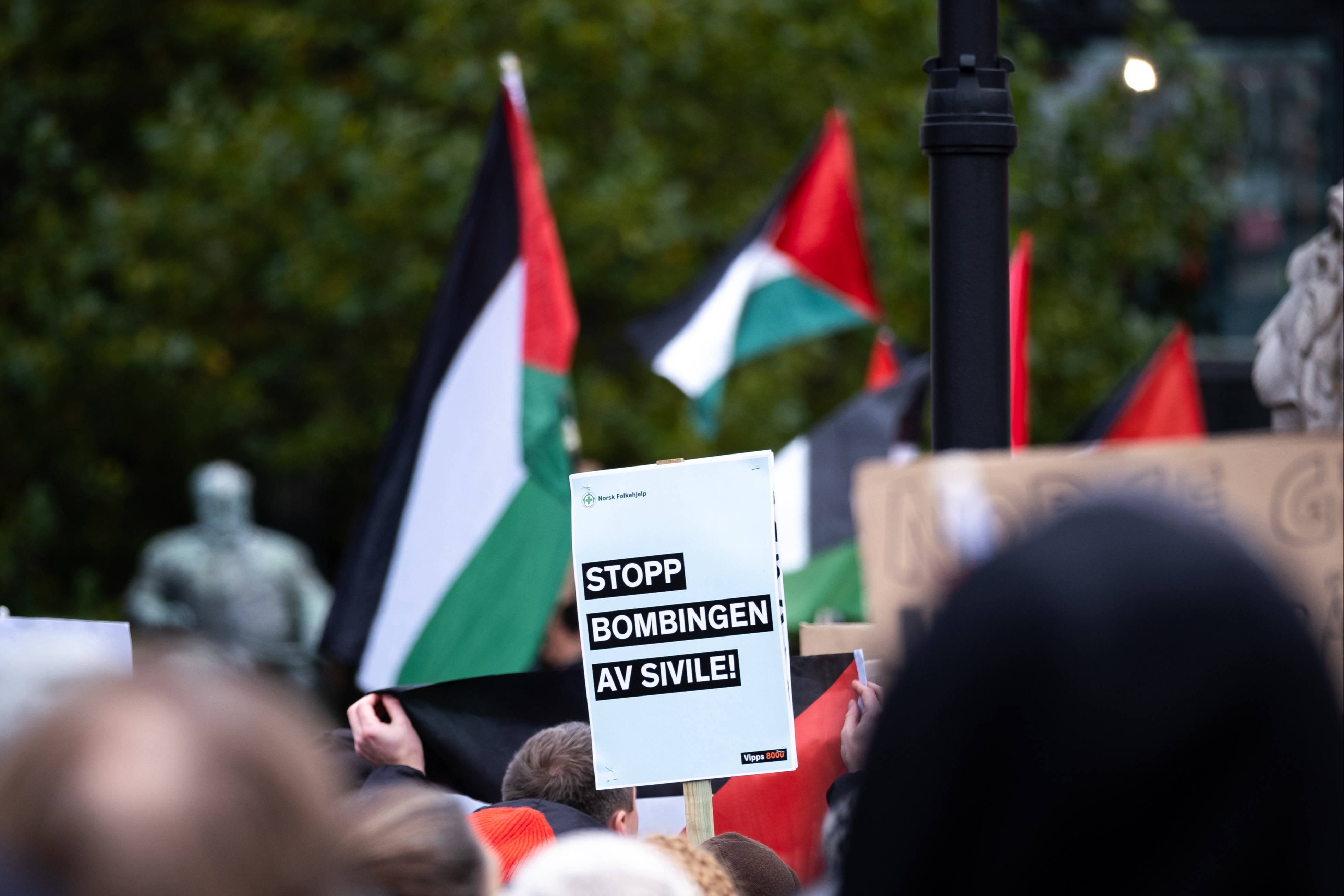 Bilde fra demonstrasjon av en plakat hvor det står "Stopp bombingen av sivile".